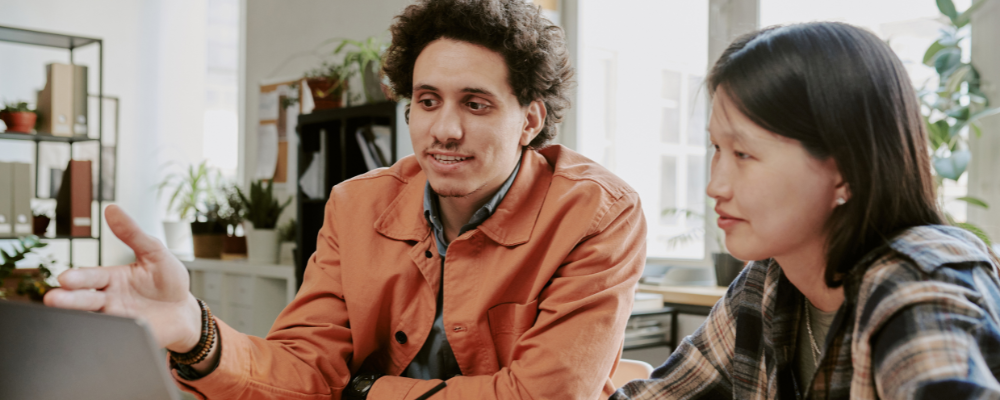 This image show's a man and woman talking at a laptop in a business scenario.